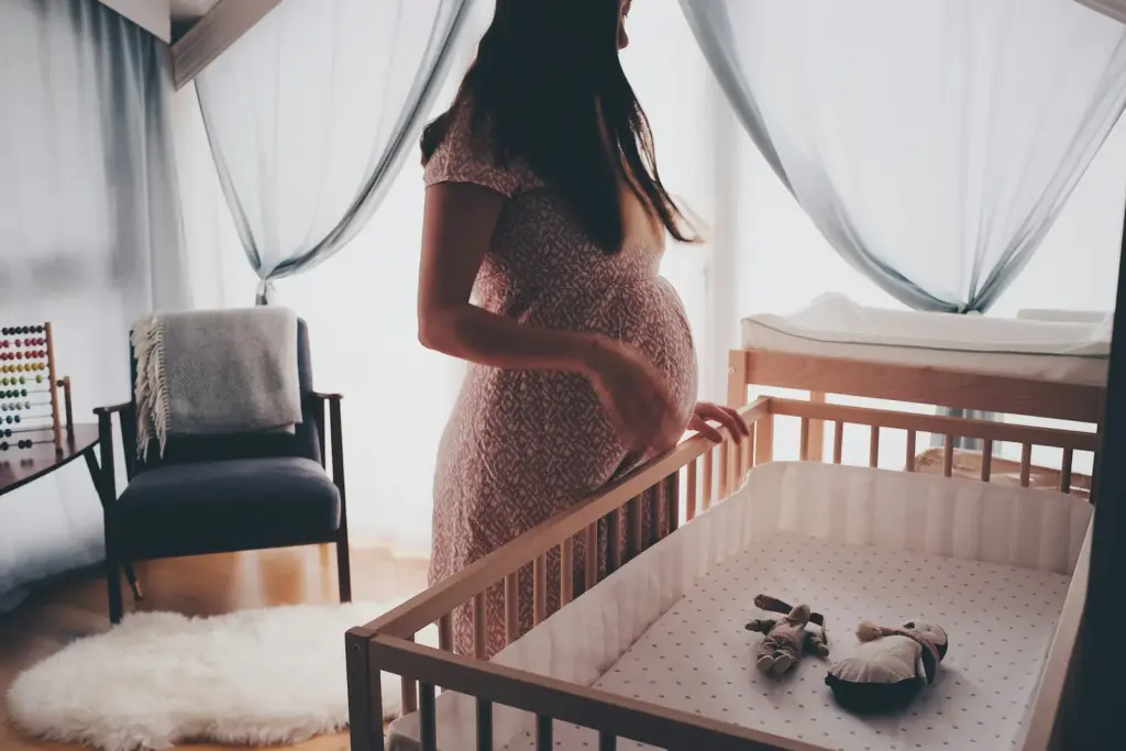 Pregnant woman standing in a sunlit nursery beside a crib