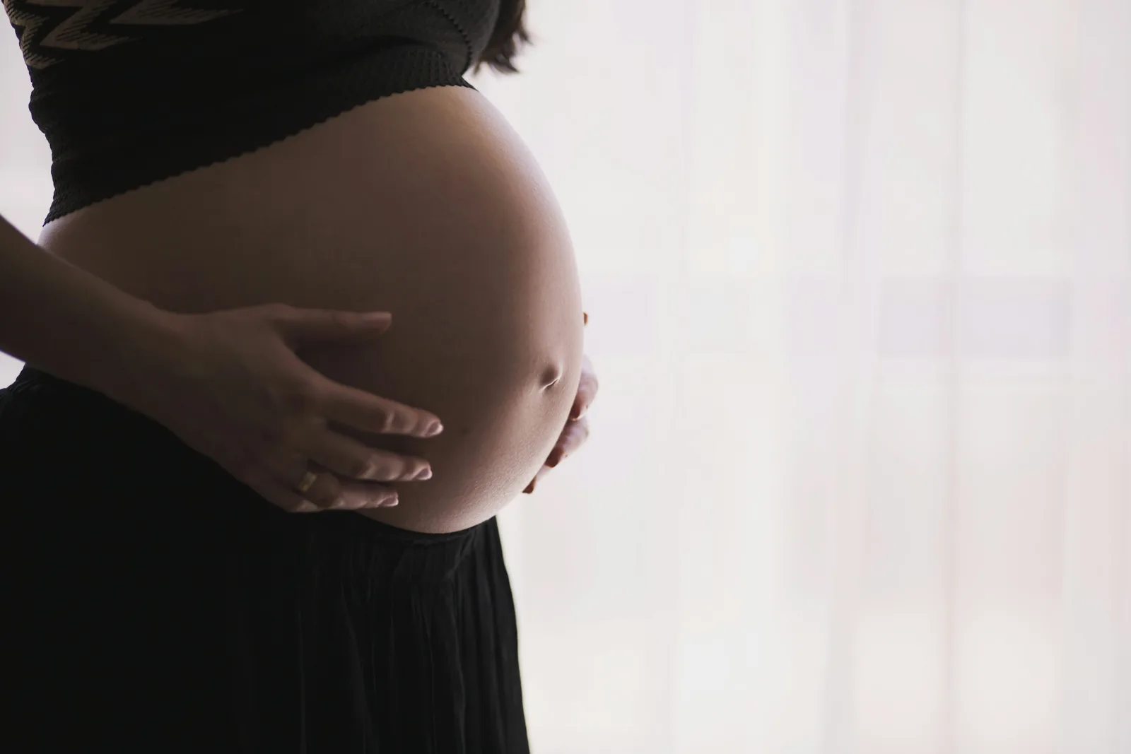 Silhouette of a pregnant woman cradling her bump beside a softly lit window